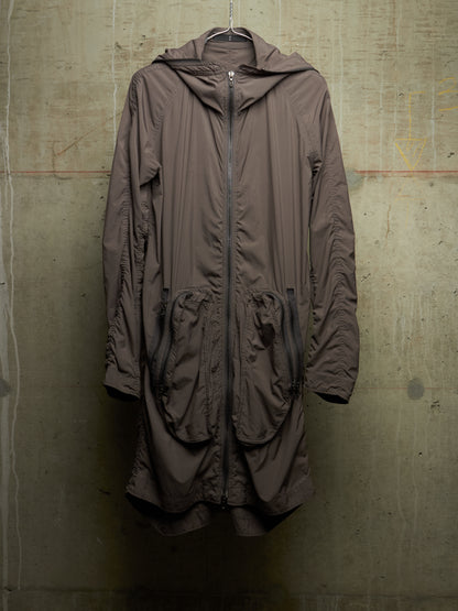 A hooded zip-front jacket in a muted taupe-brown color, hanging against a textured concrete wall.