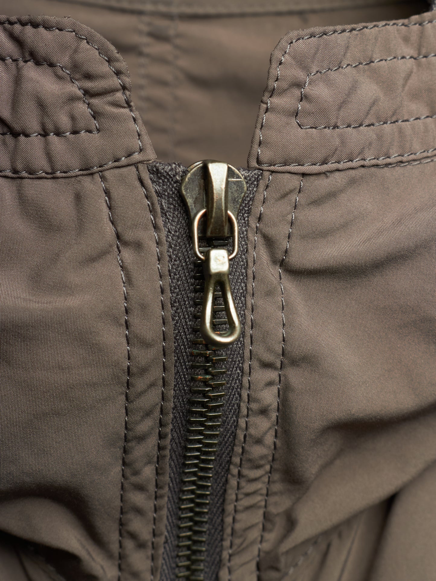 Close-up of a dark brown nylon jacket with a central metal zipper and a silver lobster clasp.