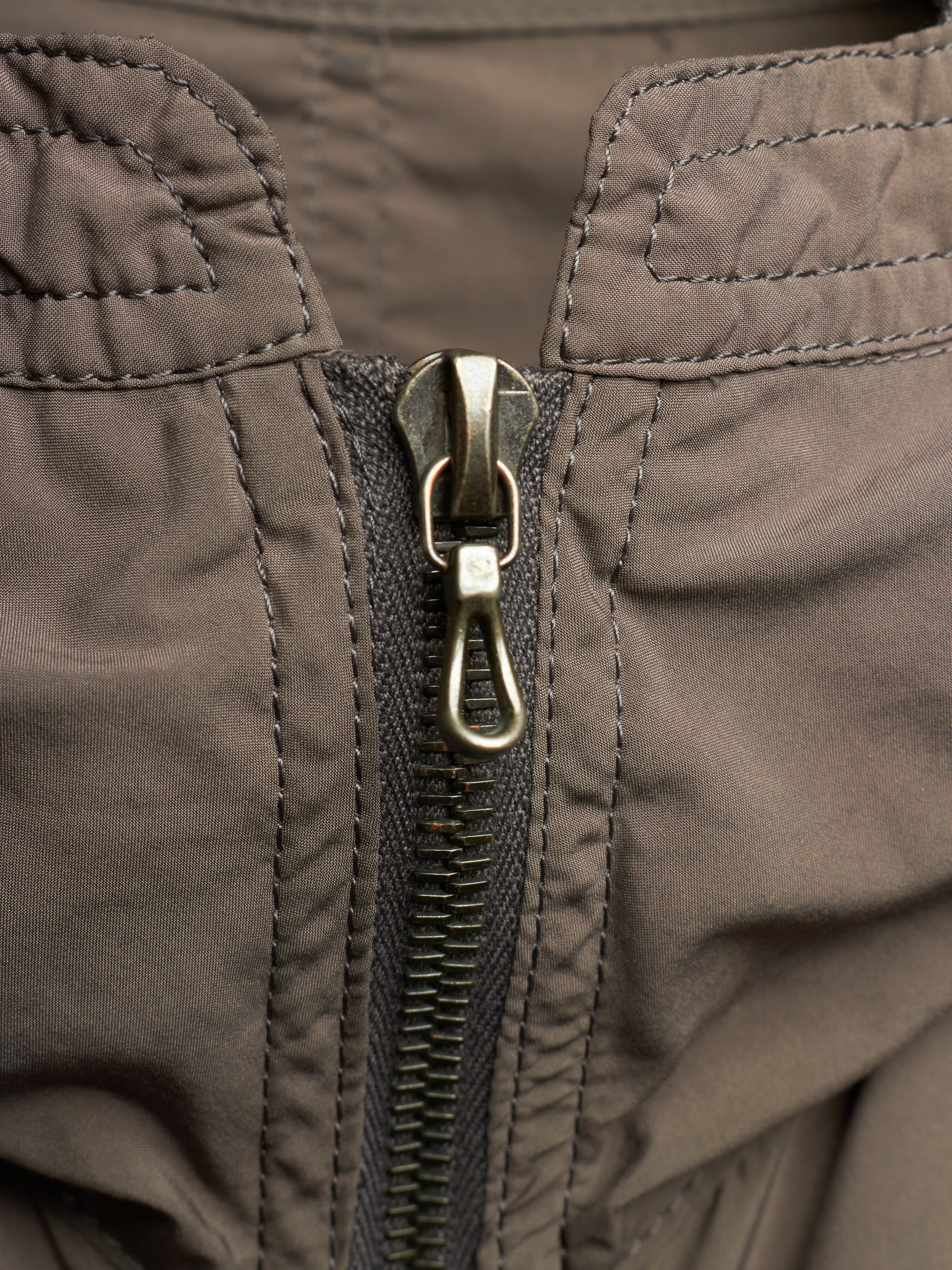 Close-up of a dark brown nylon jacket with a central metal zipper and a silver lobster clasp.