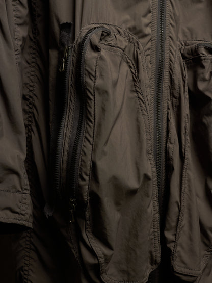 Close-up of a dark olive-brown technical jacket with multiple zippered pockets and stitched panel details.