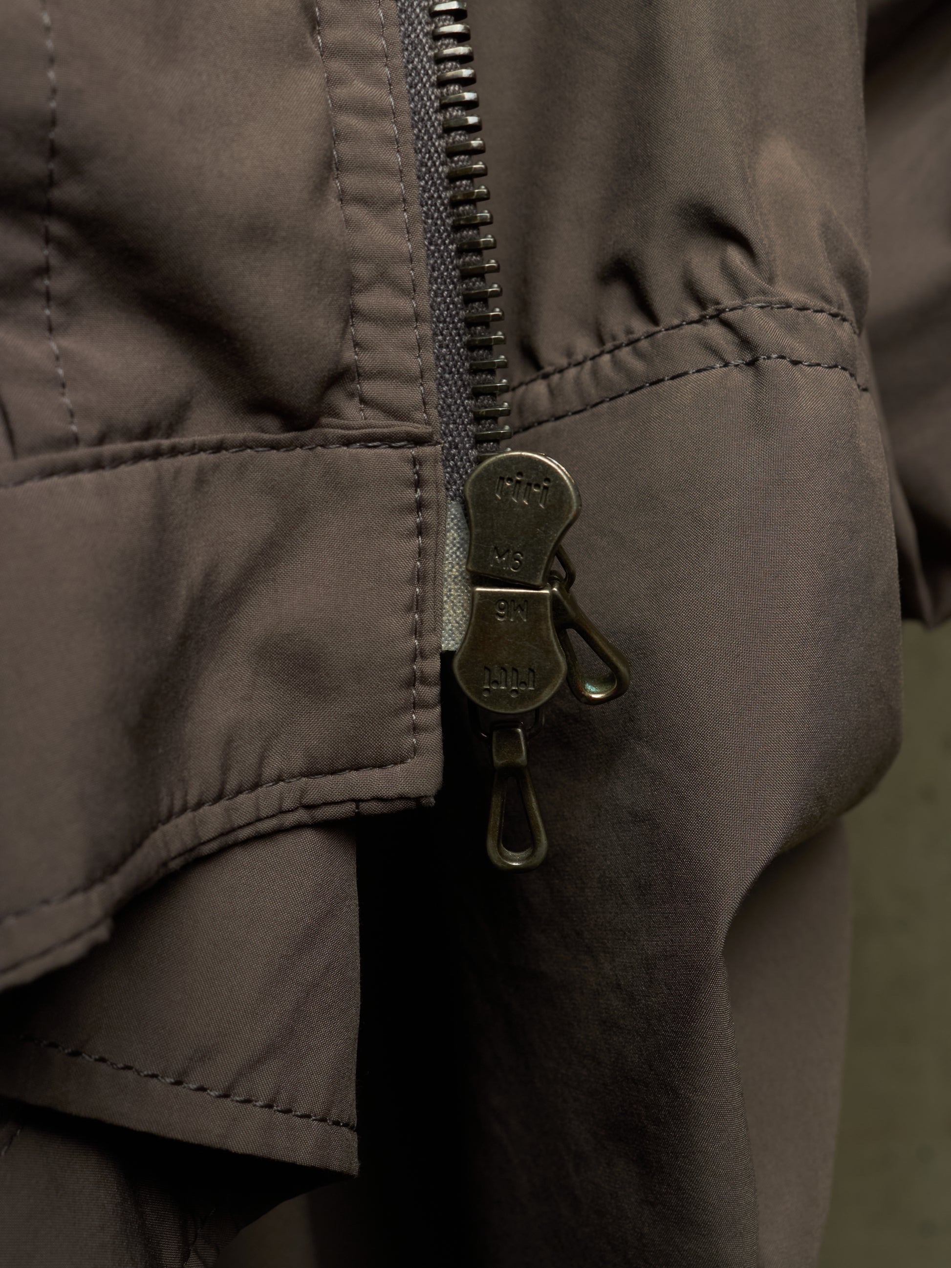 Close-up of a dark brown puffer jacket showing a metal zipper with a decorative pull tab and stitched details.