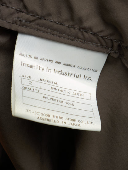 Close-up of a garment's interior label reading 'Insanity In Industrial Inc.' with size, material, and polyester details, attached to dark brown fabric.