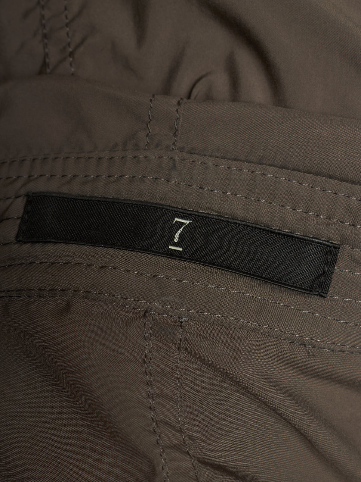 Close-up of a dark brown or taupe fabric garment with a black woven label featuring a white stylized number 7.