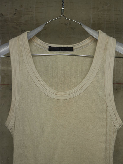 A cream-colored ribbed knit tank top hanging on a silver metal hanger against a textured concrete wall.