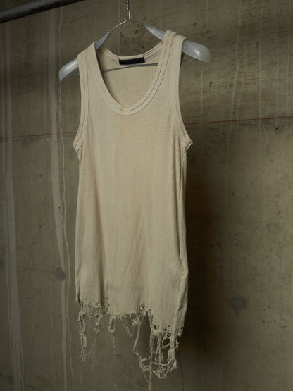 A cream-colored, sleeveless distressed tank top with frayed edges, hanging on a white plastic hanger against a textured concrete wall.