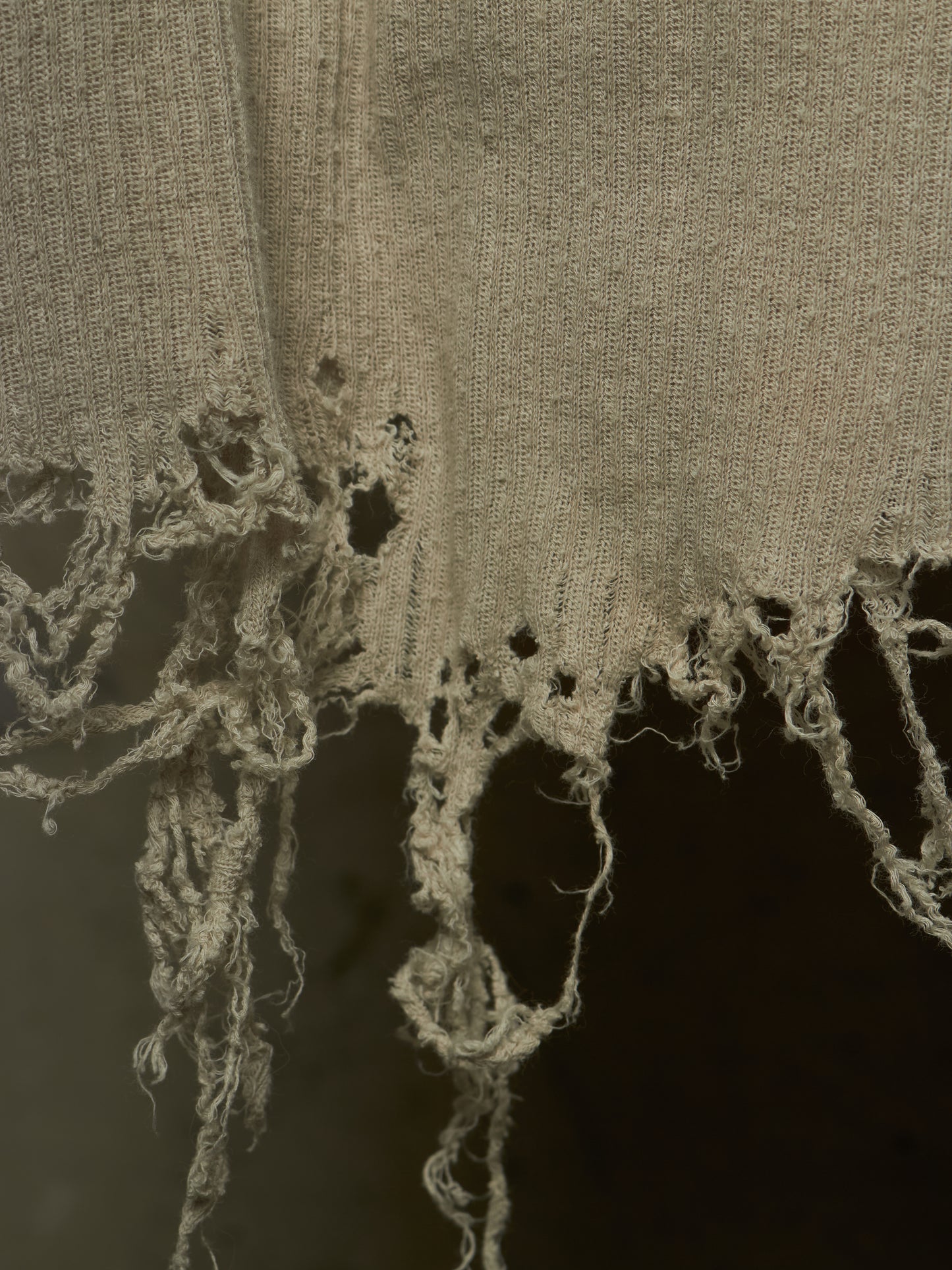 Close-up of a distressed, frayed beige fabric with rough, tattered edges against a dark background.