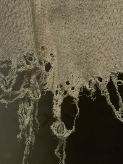 Close-up of a distressed, frayed beige fabric with rough, tattered edges against a dark background.