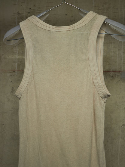 A cream-colored ribbed knit tank top hanging on a clear plastic hanger against a textured concrete wall.