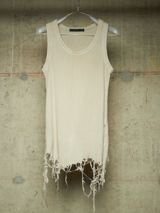 A cream-colored sleeveless knit top with a raw, frayed hem, hanging on a white hanger against a textured concrete wall.
