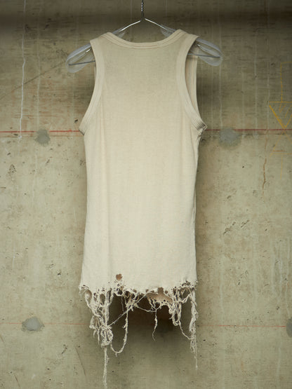 A sleeveless cream-colored tank top with a heavily distressed, frayed hem, hanging on a clear plastic hanger against a textured concrete wall.