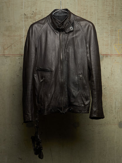 A dark brown leather motorcycle jacket hanging on a metal hanger against a textured concrete wall.