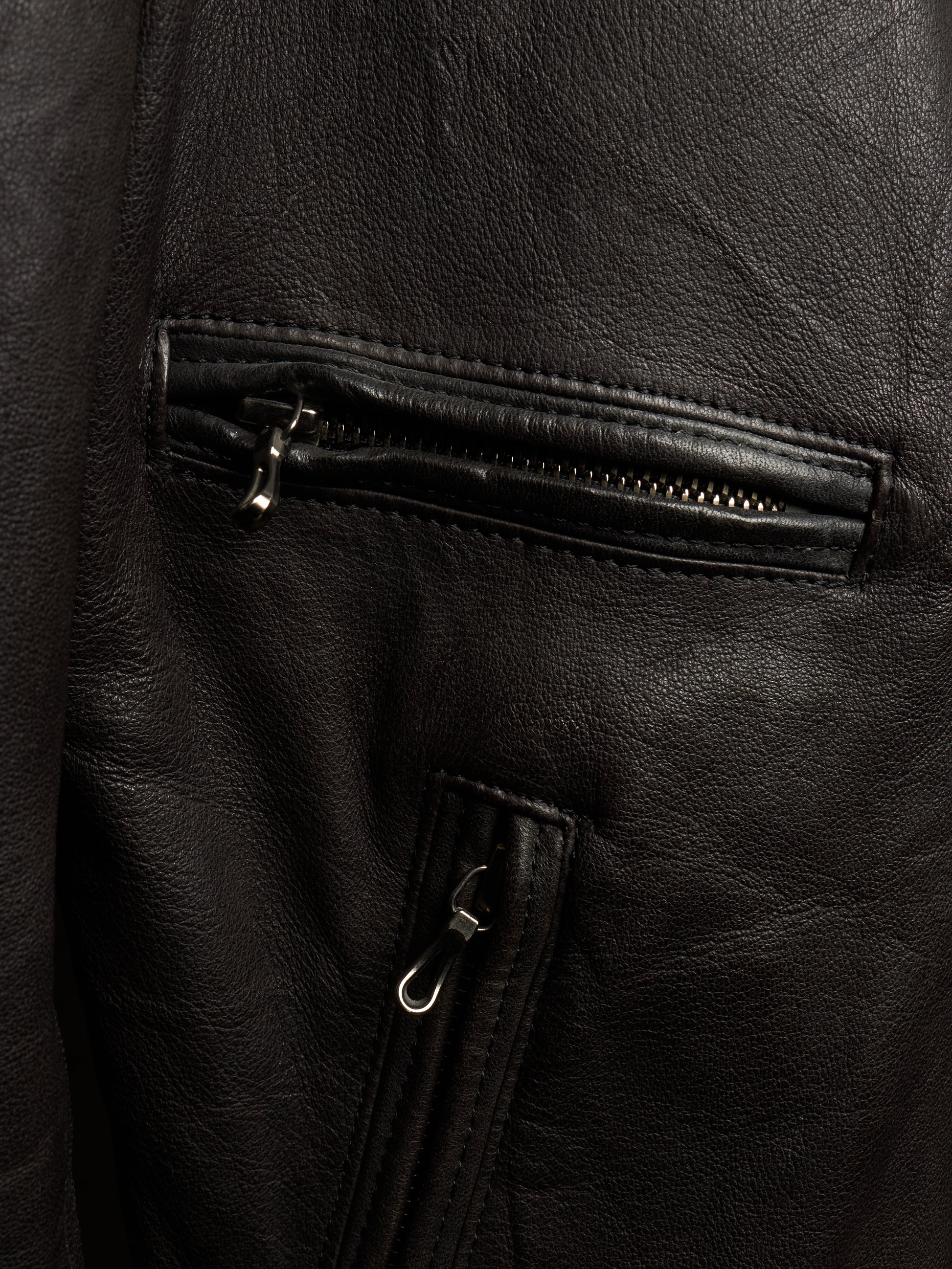 Close-up of a black leather jacket showing a zippered pocket and a vertical zip detail with silver-toned hardware.