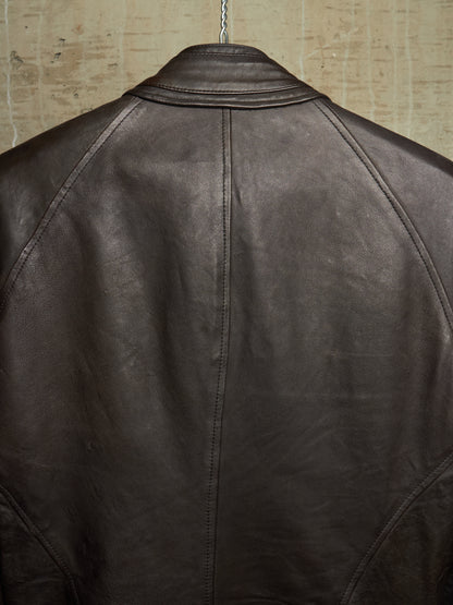Close-up back view of a dark brown leather jacket hanging against a textured beige wall.