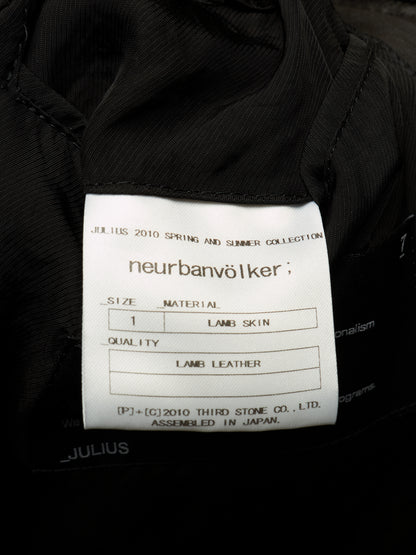 Close-up of a white fabric product label sewn onto a black garment, showing the brand name 'neurbanvölker' and text for Julius 2010 Spring and Summer Collection, size 1, lamb skin, and lamb leather.