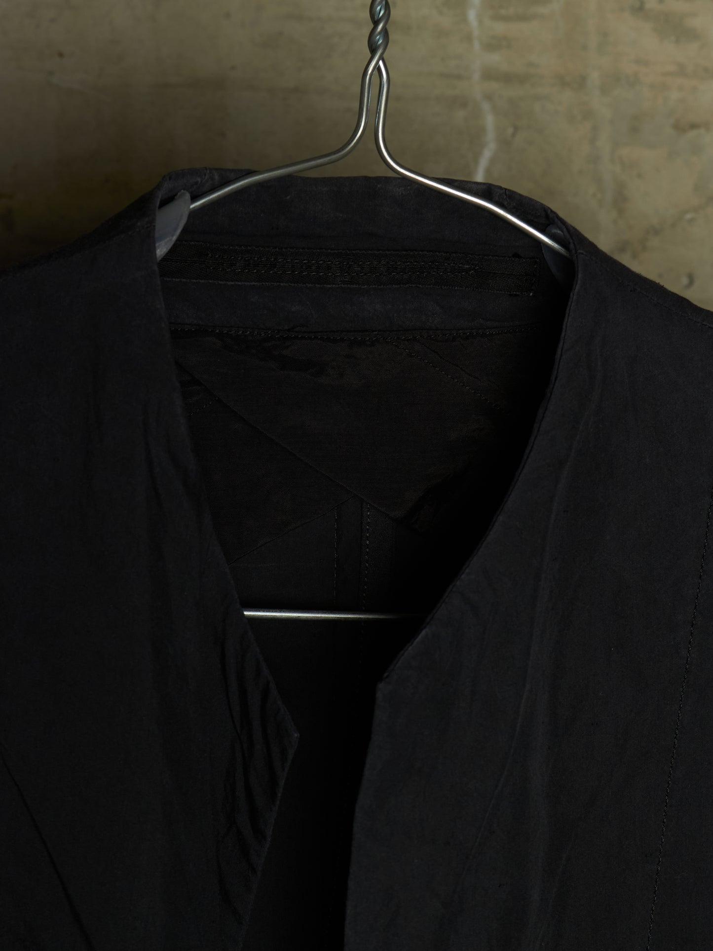 A close-up of a black garment hanging on a metal hanger against a textured beige wall.