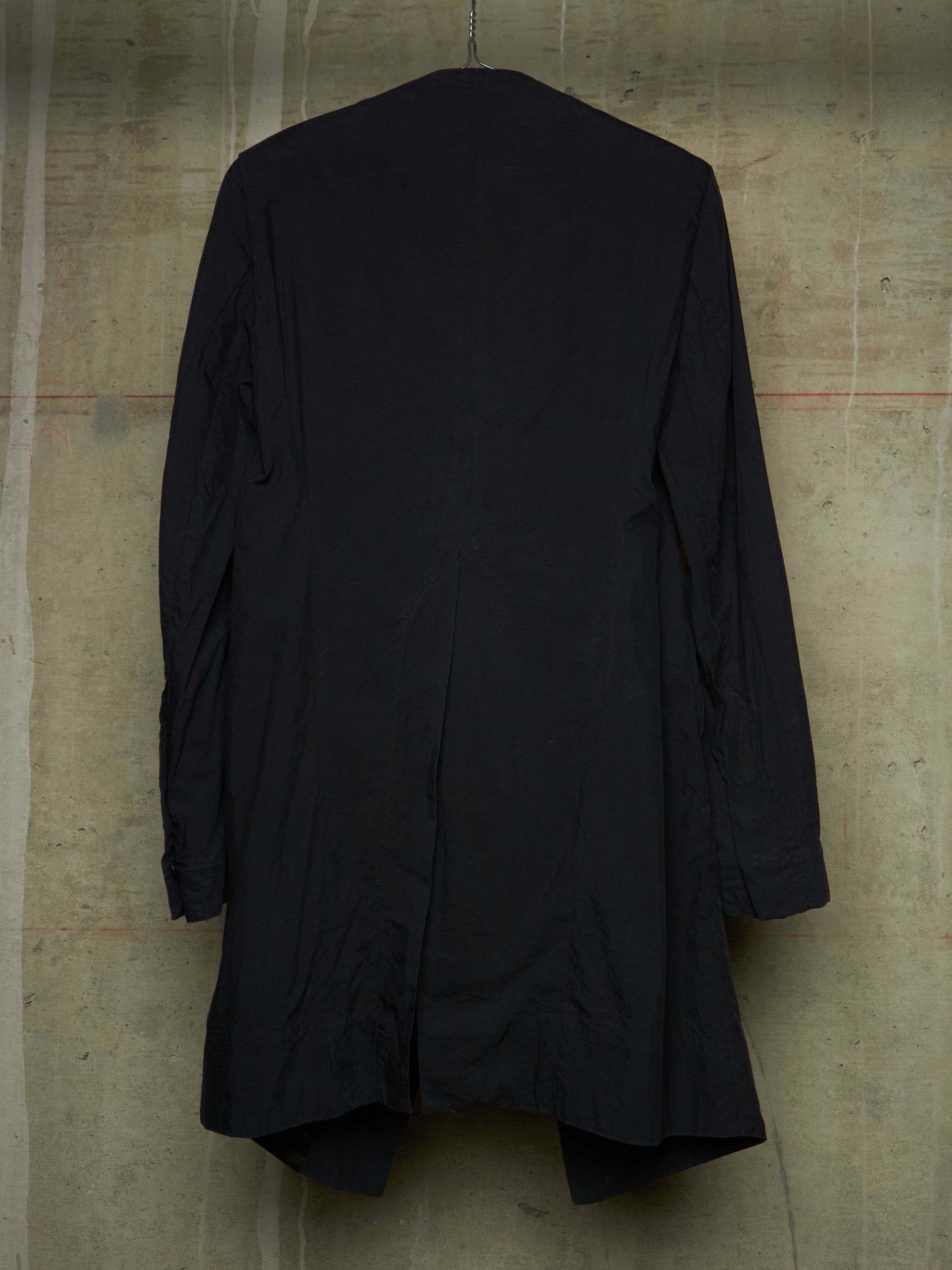 A black long-sleeve coat or jacket hanging against a textured concrete wall, shown from the back.