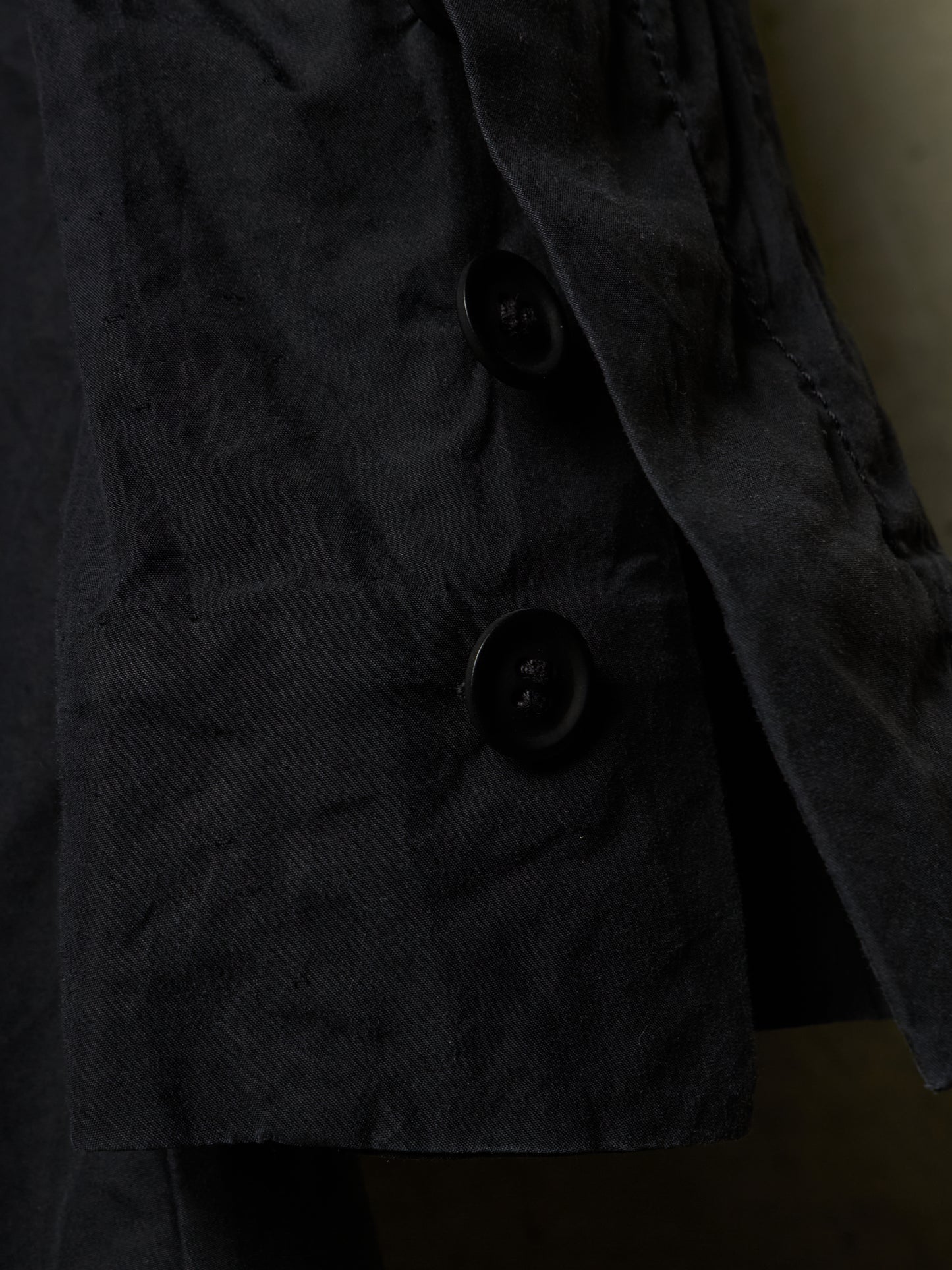 Close-up of a dark charcoal gray textured jacket with black buttons, showing the fabric texture and stitching details.
