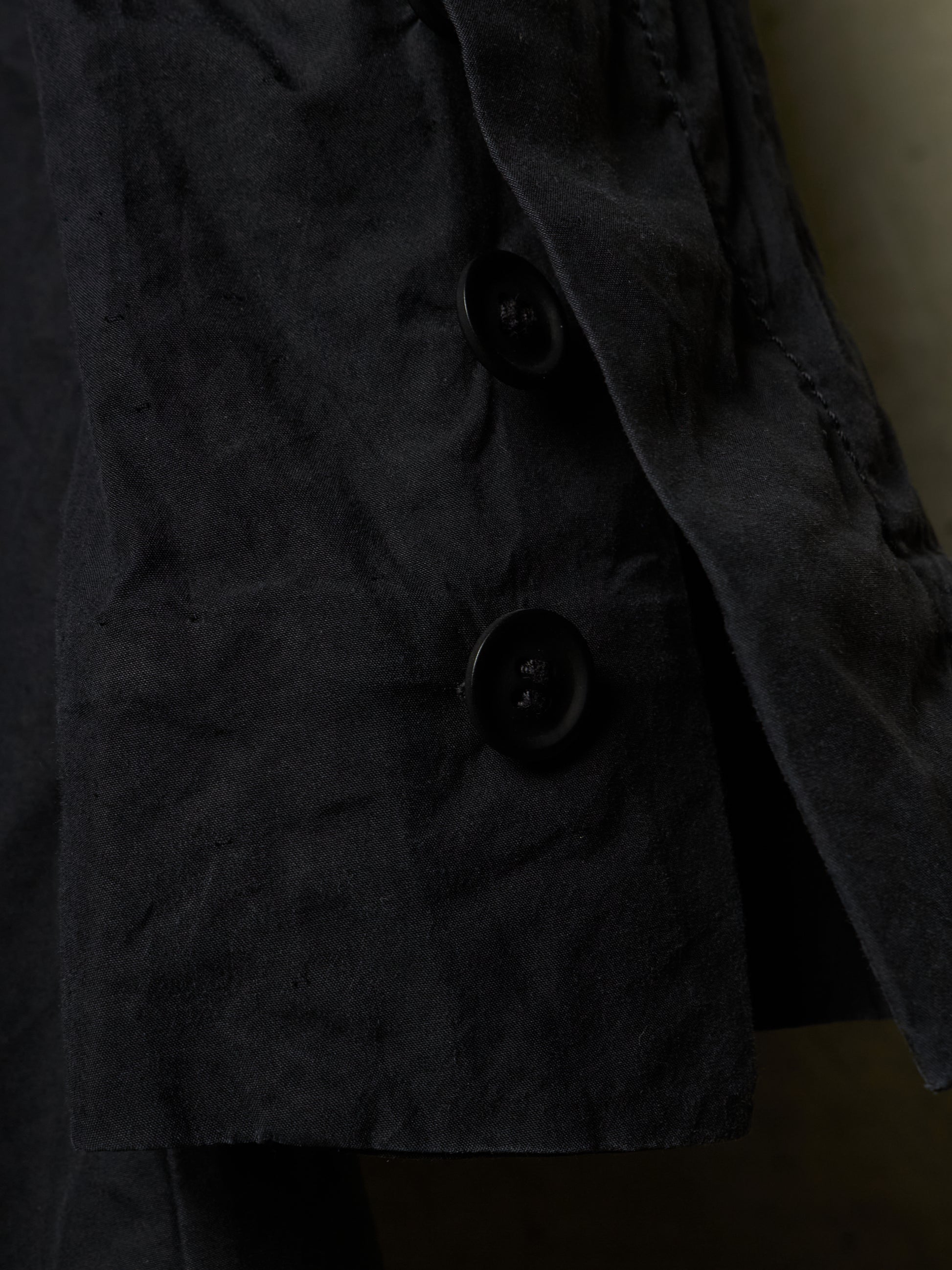 Close-up of a dark charcoal gray textured jacket with black buttons, showing the fabric texture and stitching details.