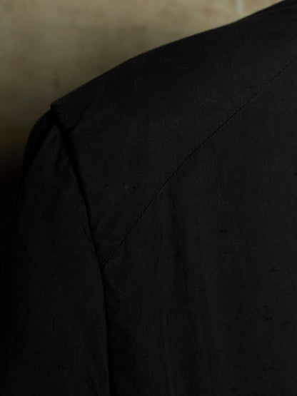 Close-up detail of a black garment, showing the shoulder seam and textured fabric against a dark background.