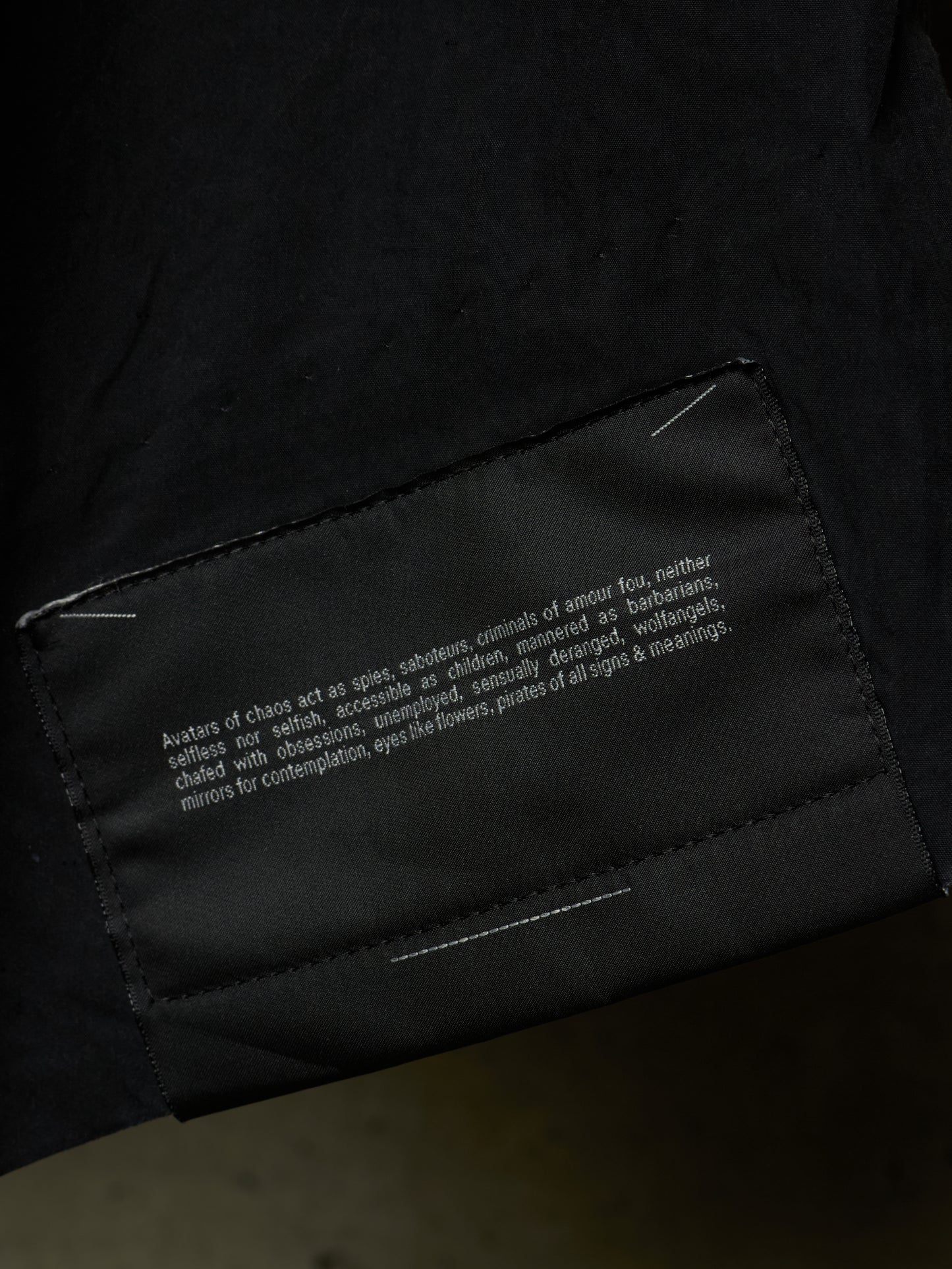 Close-up of a black garment showing a sewn-in fabric label with white text on the inside of a sleeve or cuff.