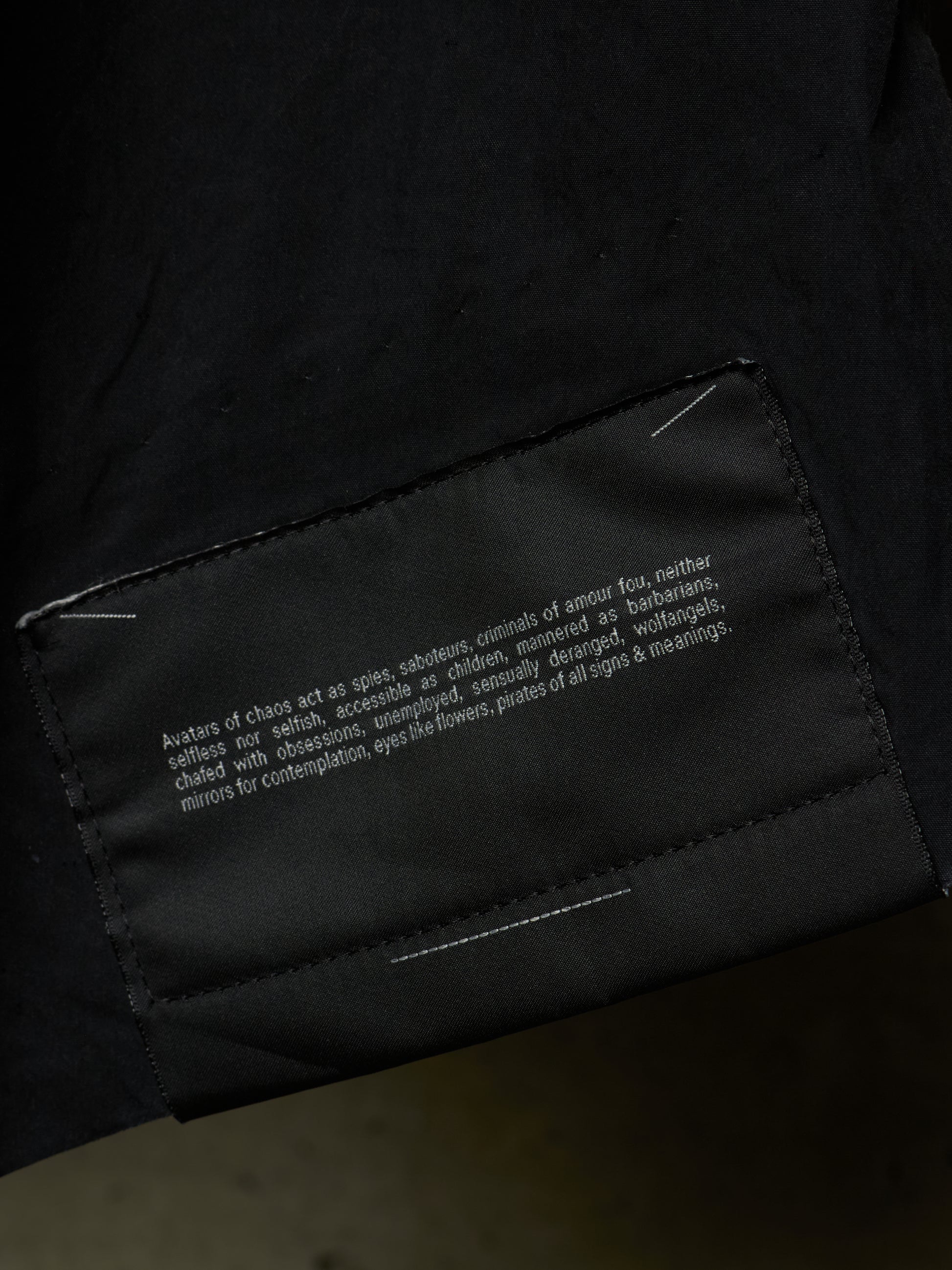 Close-up of a black garment showing a sewn-in fabric label with white text on the inside of a sleeve or cuff.