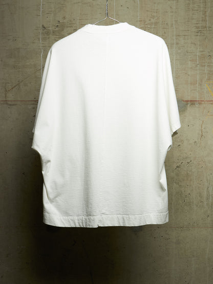 A white oversized short-sleeve t-shirt hanging on a wire hanger against a textured concrete wall.