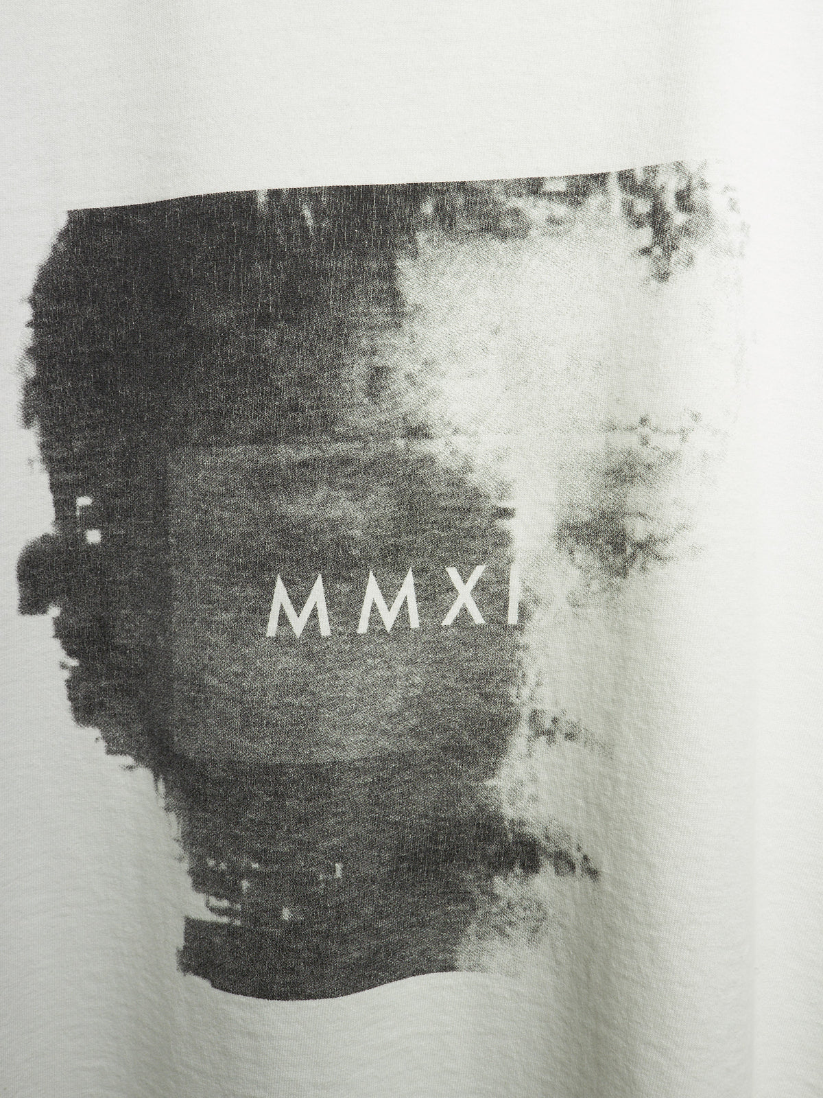 Close-up of a white garment featuring a large black abstract paint-splatter graphic with the Roman numerals 'MMXI' printed in white across the center.