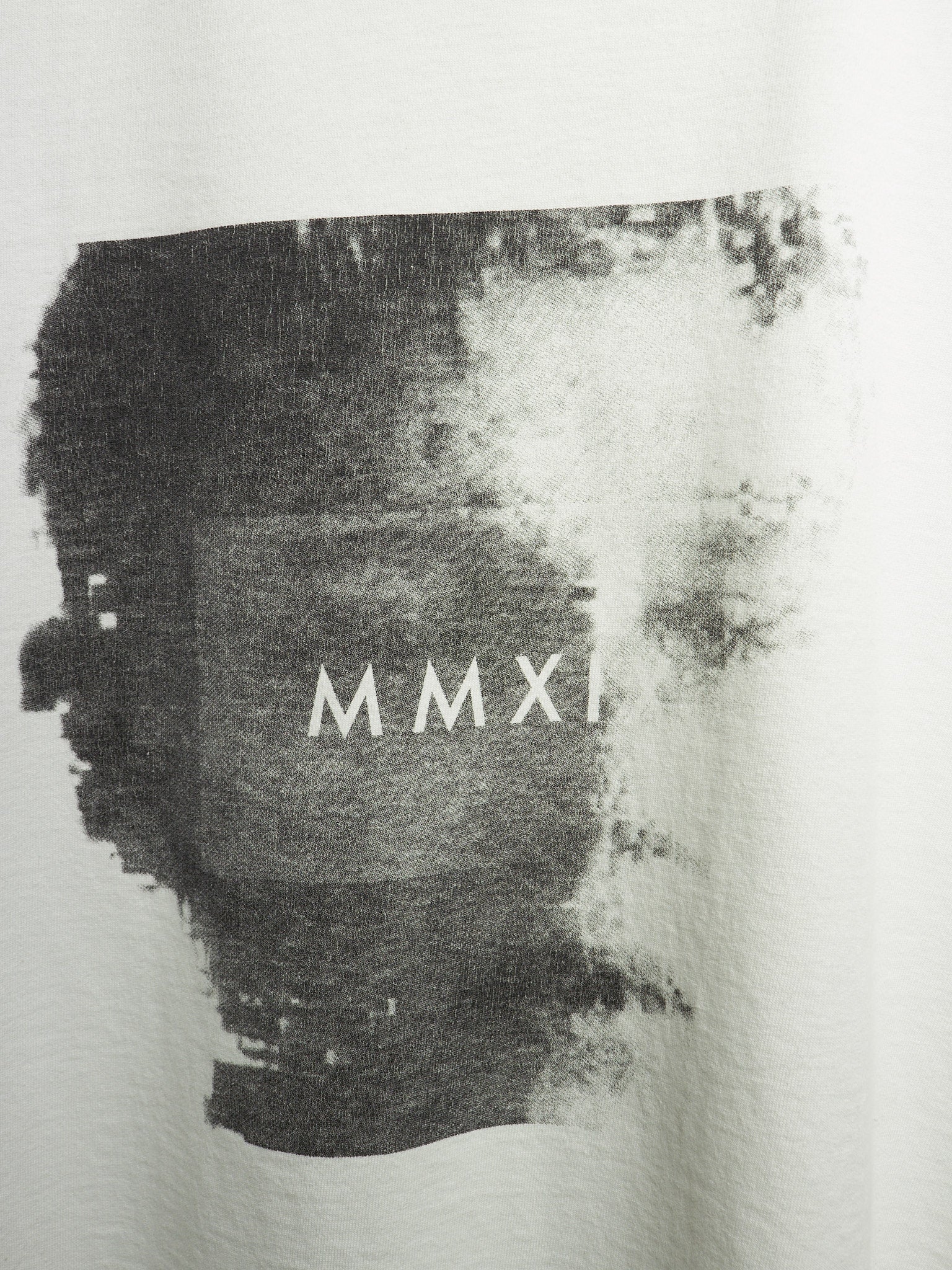 Close-up of a white garment featuring a large black abstract paint-splatter graphic with the Roman numerals 'MMXI' printed in white across the center.