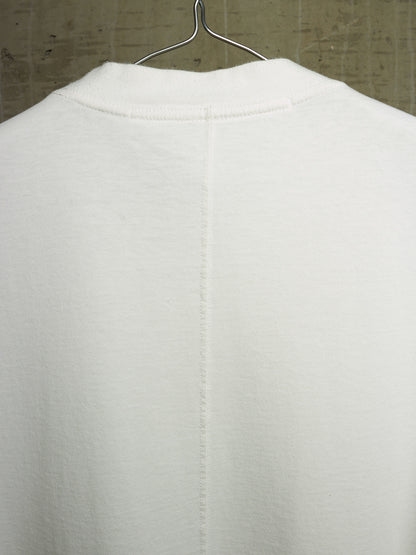 A close-up of the back of a white knit garment hanging on a metal hanger against a textured gray wall.