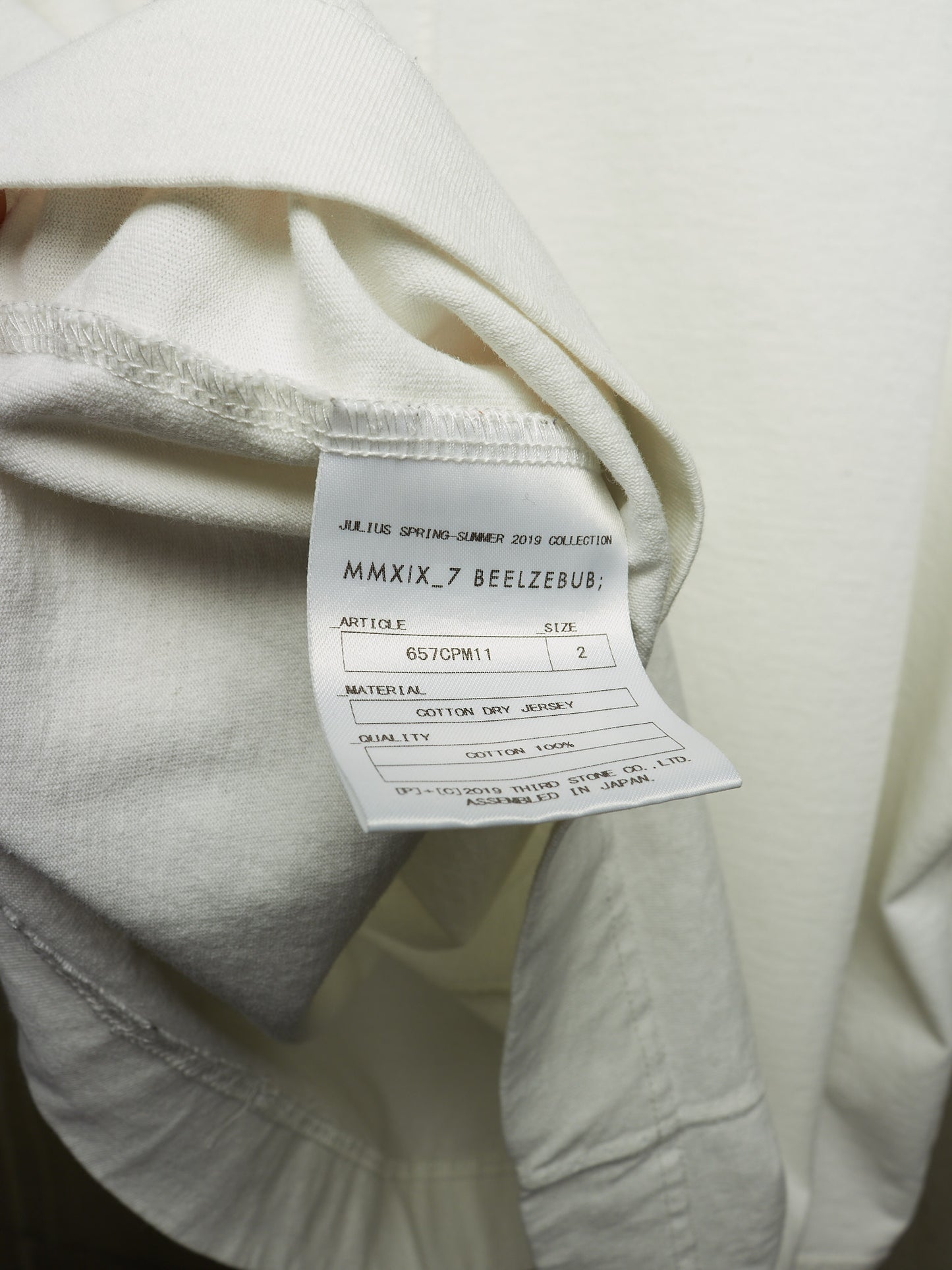 Close-up of a cream-colored garment showing the inner neck label with text including 'JEANS SPRING-SUMMER COLLECTION MMXIX.7 BEEZBUB'.