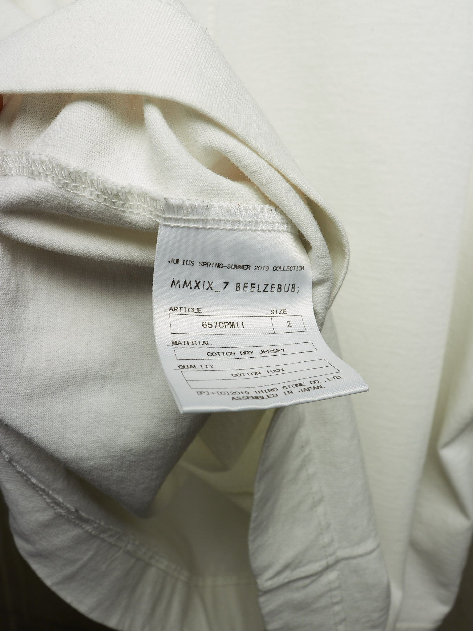 Close-up of a cream-colored garment showing the inner neck label with text including 'JEANS SPRING-SUMMER COLLECTION MMXIX.7 BEEZBUB'.
