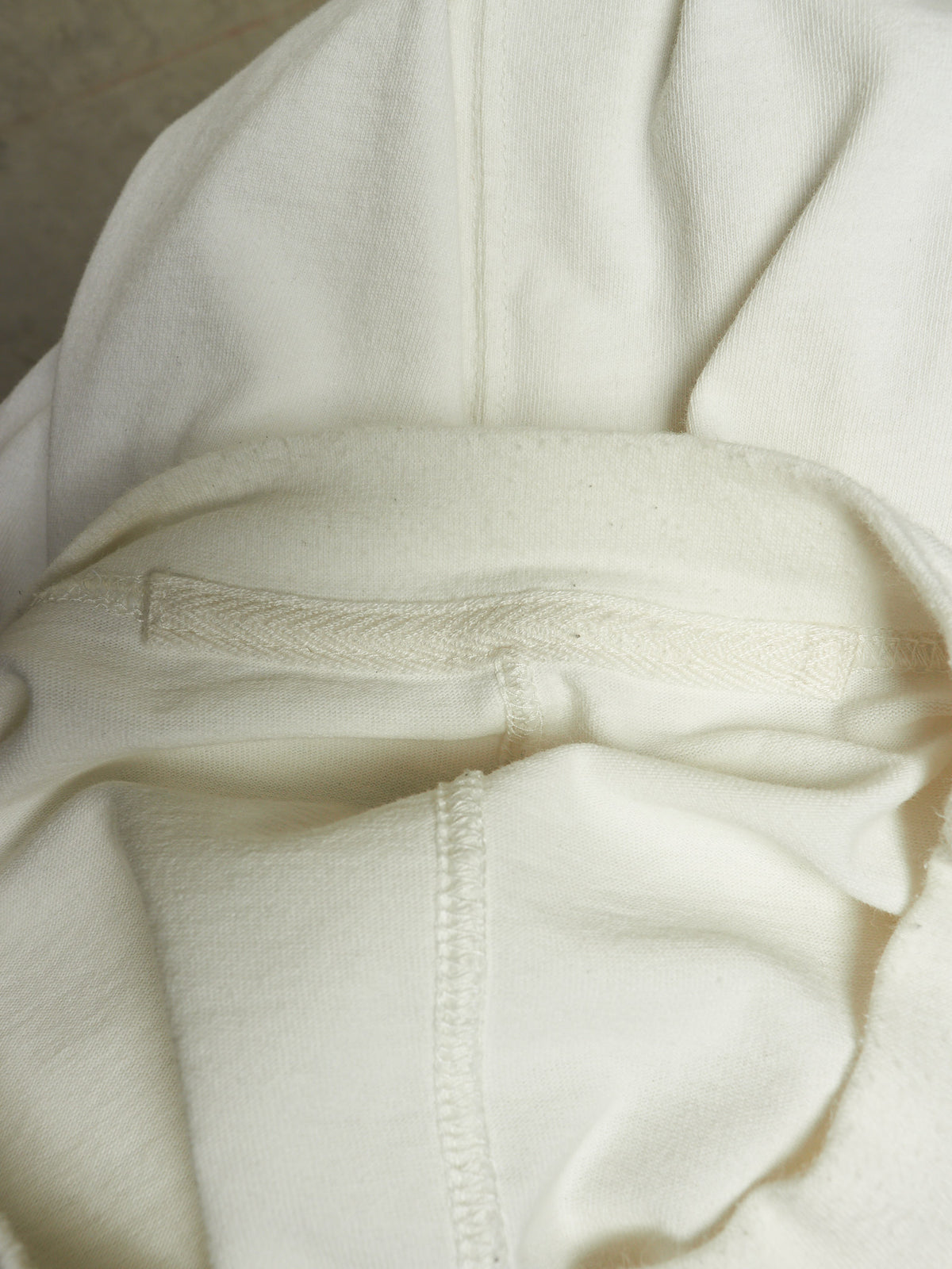 Close-up of a cream-colored knit garment, showing the texture of the fabric, a horizontal ribbed band, and a vertical seam.