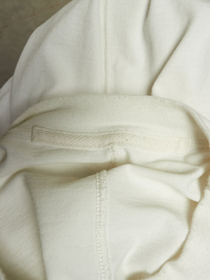 Close-up of a cream-colored knit garment, showing the texture of the fabric, a horizontal ribbed band, and a vertical seam.