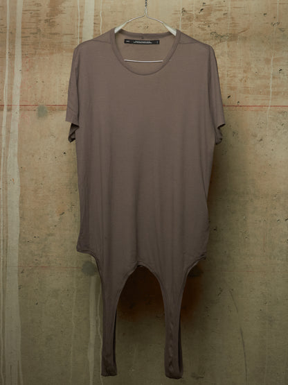 A taupe-brown short-sleeve tunic top with a split leg design, hanging on a white hanger against a textured concrete wall.