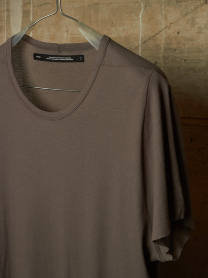 A taupe brown short-sleeve knit top hanging on a metal hanger against a textured stone wall background.