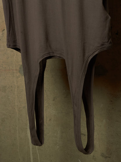 A dark brown ribbed bodysuit or long-sleeve top with split leg openings, hanging against a textured concrete wall.