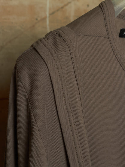 Close-up of a ribbed knit top in taupe brown, showing the shoulder seam and collar area against a warm beige background.