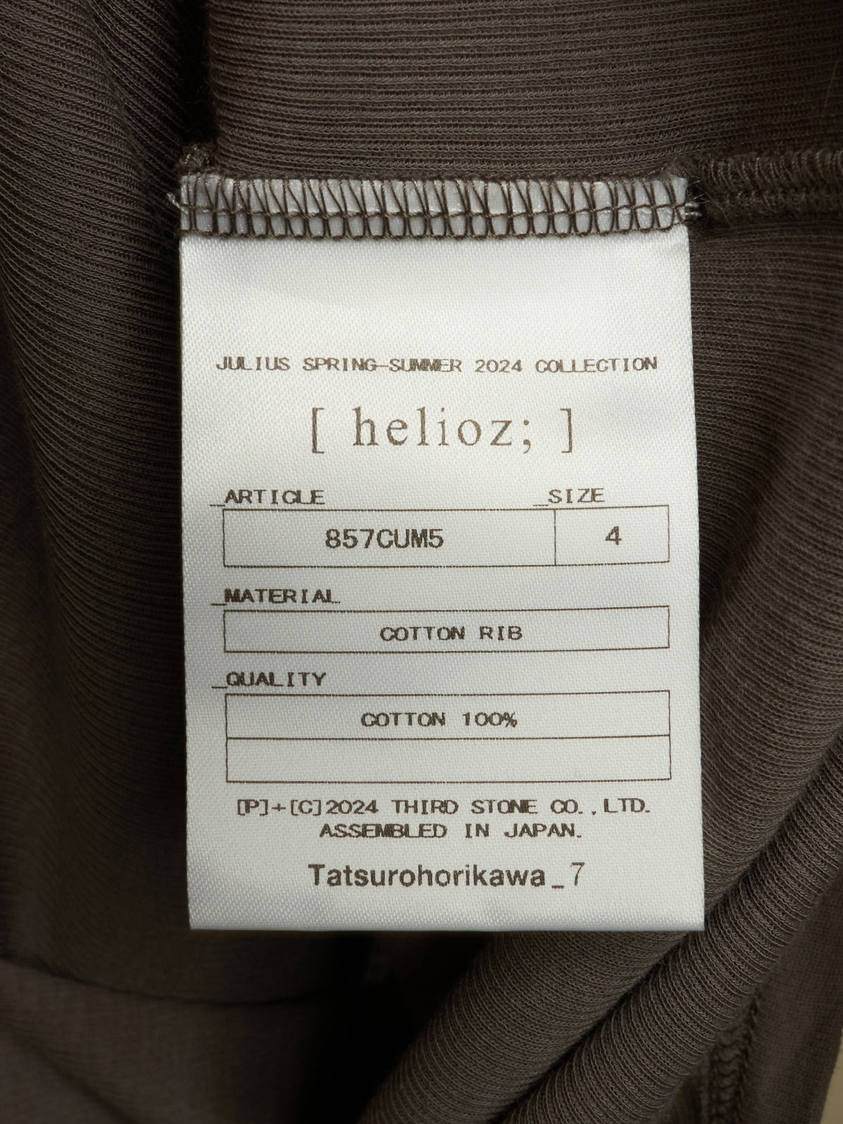 A close-up of a garment's interior label reading 'helioz;' and 'Julius Spring-Summer 2024 Collection,' with details including article number 857CUM5, size 4, cotton rib material, and cotton 100% quality.