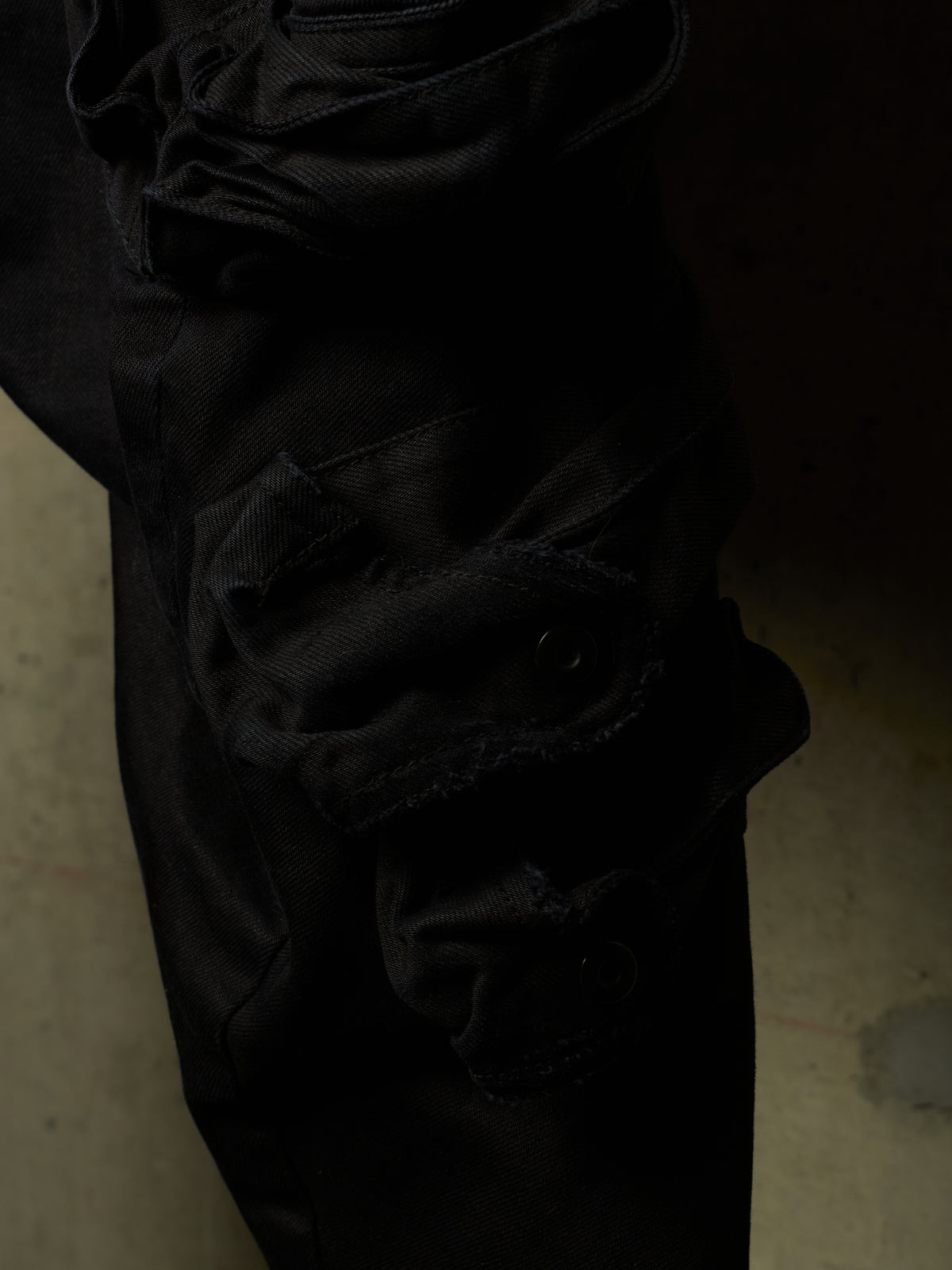 Close-up of black distressed cargo pants showing a heavily frayed, ripped knee patch and layered fabric details.