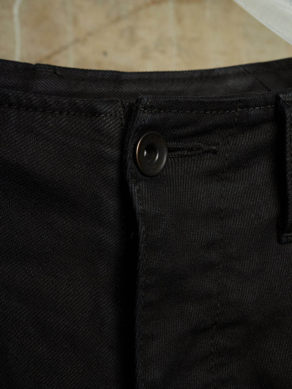 Close-up detail of black denim pants showing the button closure, belt loop, and fabric texture.