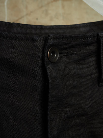 Close-up detail of black denim pants showing the button closure, belt loop, and fabric texture.