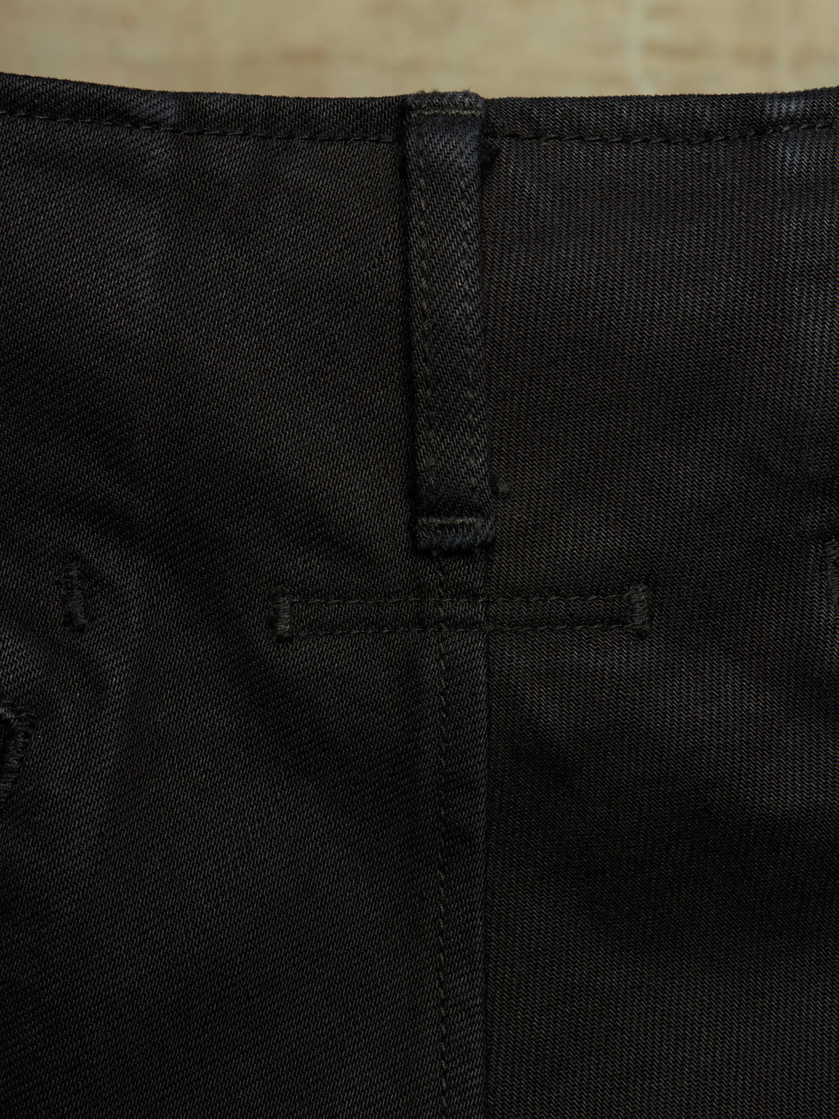 Close-up detail of black denim fabric showing the back waistband, belt loop, and stitching.