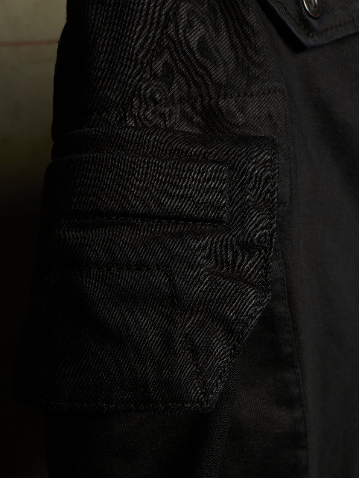Close-up detail of a black canvas utility jacket, showing a buttoned flap pocket and stitched fabric texture.