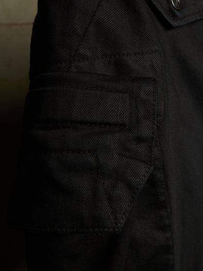 Close-up detail of a black canvas utility jacket, showing a buttoned flap pocket and stitched fabric texture.