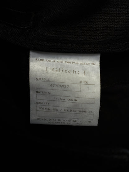 A close-up of a white fabric product label inside a black garment, showing the brand name 'Glitch;' and product details.