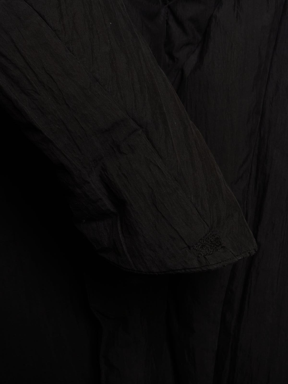 Close-up detail of a black crinkled fabric garment, showing a sleeve and draped material texture.