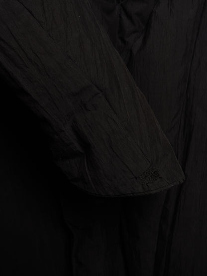 Close-up detail of a black crinkled fabric garment, showing a sleeve and draped material texture.