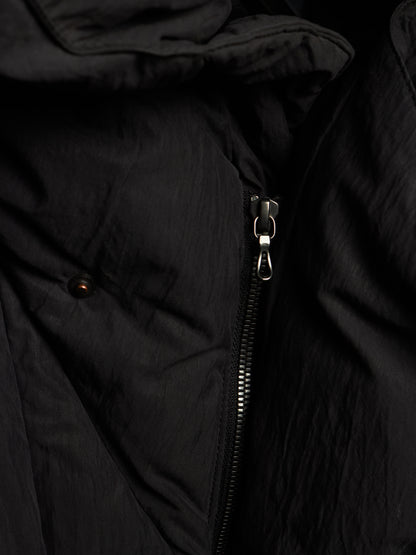Close-up of a black puffer jacket showing the textured crinkled fabric, a silver metal zipper, and a small dark button detail.