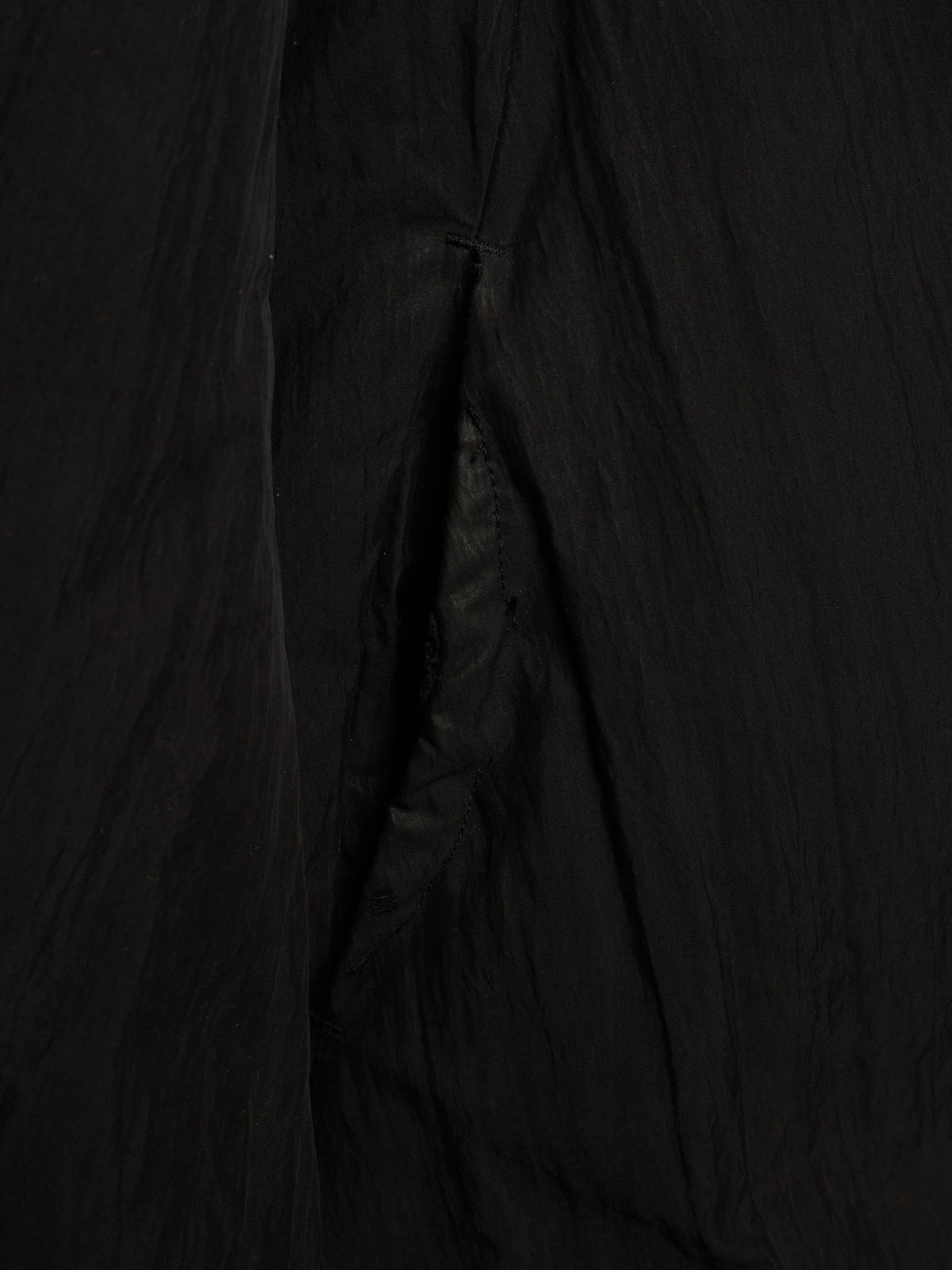 A close-up of a black crinkled fabric, showing the texture and folds of a garment or textile.