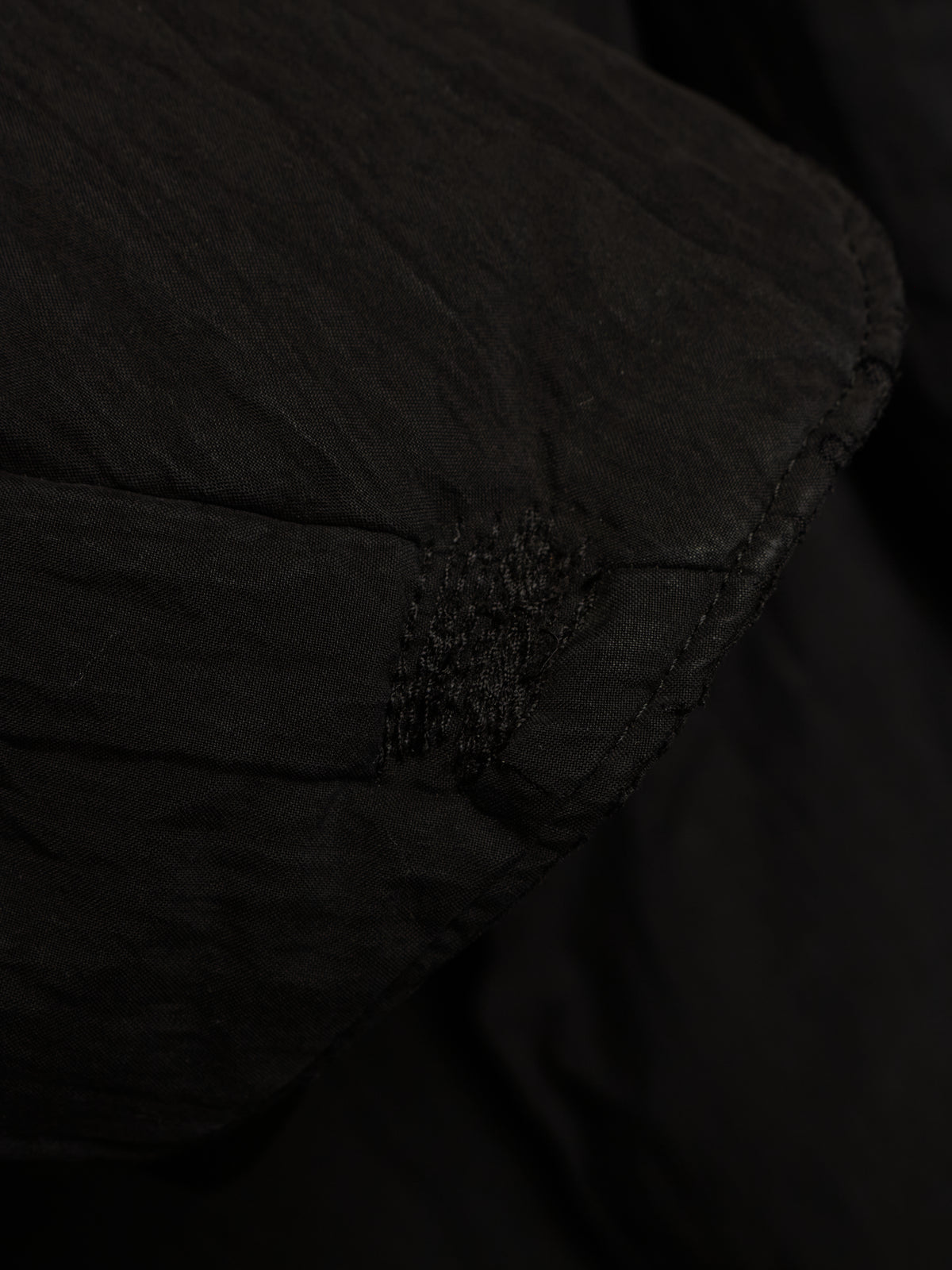 Close-up detail of a black quilted fabric item, showing stitched paneling and a small textured accent.
